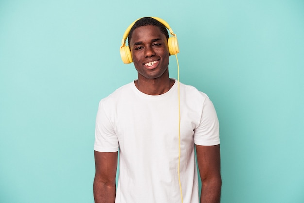 Jeune homme afro-américain écoutant de la musique isolée sur fond bleu heureux, souriant et joyeux.