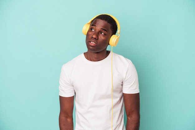 Jeune homme afro-américain écoutant de la musique isolée sur fond bleu rêvant d'atteindre des objectifs et des objectifs