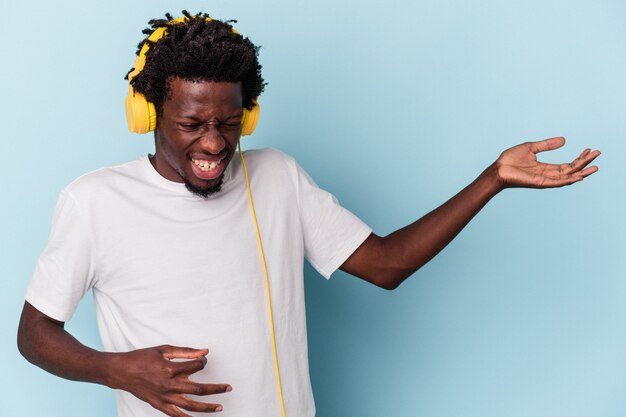 Jeune homme afro-américain écoutant de la musique isolée sur fond bleu se sent fier et confiant, exemple à suivre.