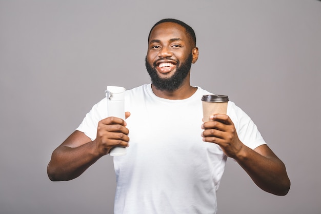 Jeune homme afro-américain faisant choisir entre une tasse de café et recycler un debout sur fond gris isolé.