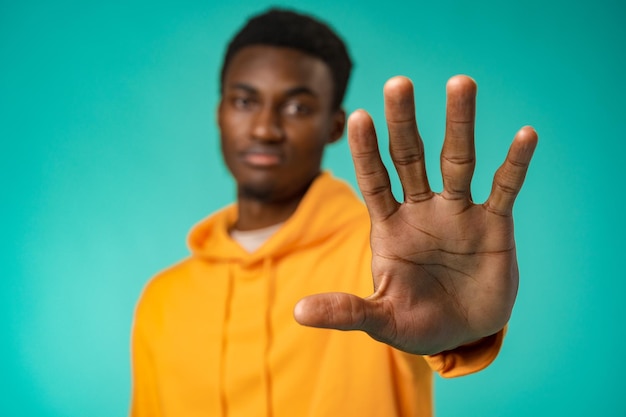 Jeune homme afro-américain sur le fond du studio faisant arrêter de chanter avec la paume de la main