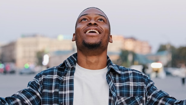 Un jeune homme afro-américain heureux dans un t-shirt décontracté isolé dans la rue de la ville à l'extérieur en regardant la caméra