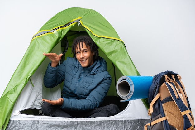 Jeune homme afro-américain à l'intérieur d'une tente de camping vert tenant un espace vide