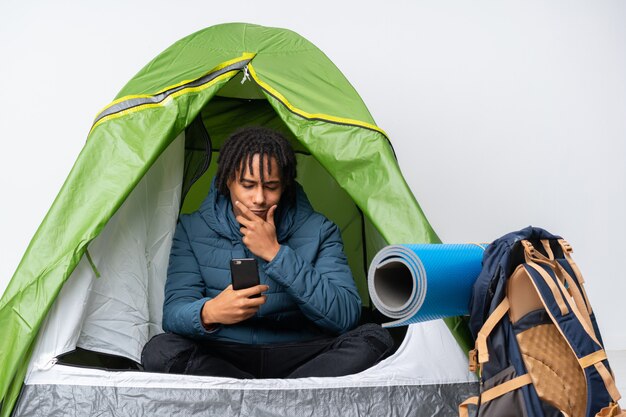 Jeune homme afro-américain à l'intérieur d'une tente verte de camping en pensant et en envoyant un message