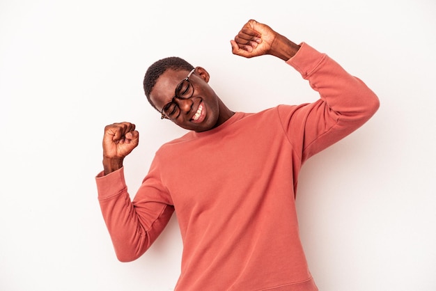 Jeune homme afro-américain isolé sur fond blanc célébrant une journée spéciale, saute et lève les bras avec énergie.