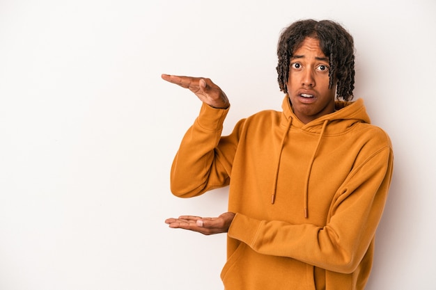 Jeune homme afro-américain isolé sur fond blanc choqué et étonné tenant un espace de copie entre les mains.