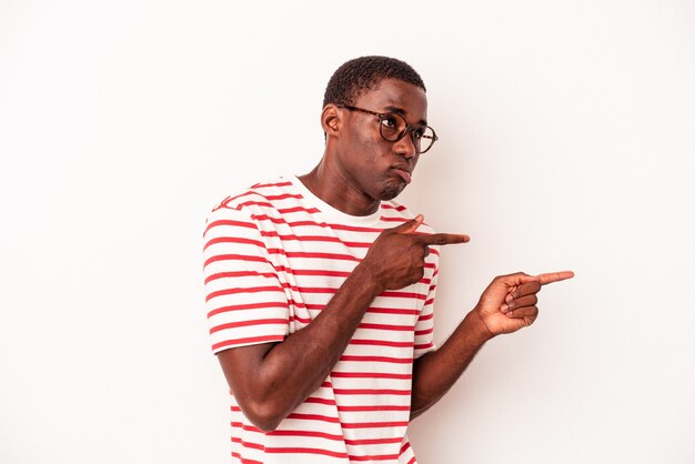 Jeune homme afro-américain isolé sur fond blanc choqué pointant avec l'index vers un espace de copie.