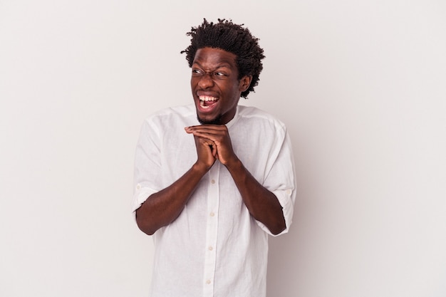 Jeune homme afro-américain isolé sur fond blanc garde les mains sous le menton, regarde joyeusement de côté.