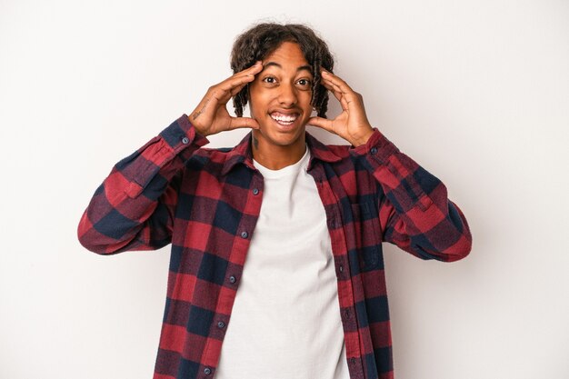 Jeune homme afro-américain isolé sur fond blanc recevant une agréable surprise, excité et levant les mains.