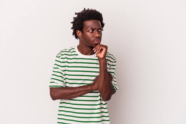 Jeune homme afro-américain isolé sur fond blanc regardant de côté avec une expression douteuse et sceptique.