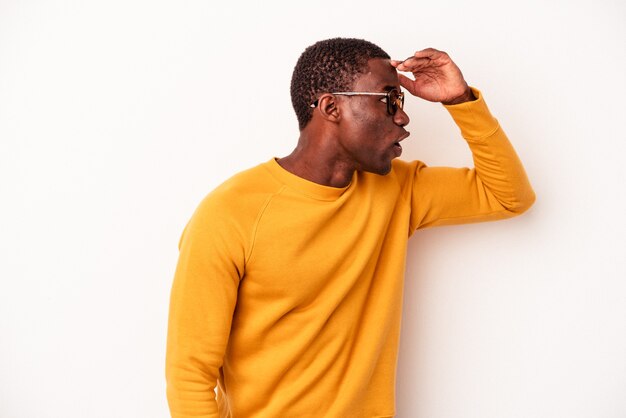 Jeune homme afro-américain isolé sur fond blanc regardant loin en gardant la main sur le front.