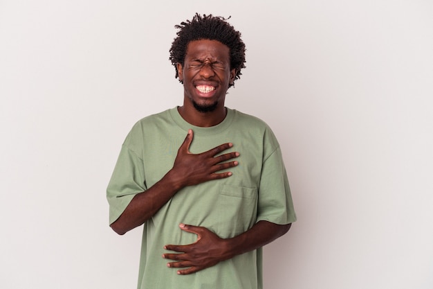 Jeune homme afro-américain isolé sur fond blanc rit joyeusement et s'amuse à garder les mains sur le ventre.