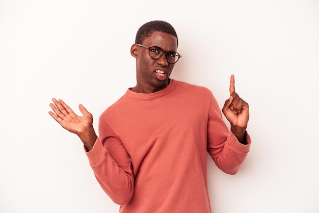 Jeune homme afro-américain isolé sur fond blanc tenant et montrant un produit à portée de main.