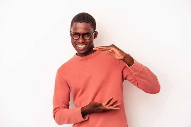 Jeune homme afro-américain isolé sur fond blanc tenant quelque chose de petit avec les index, souriant et confiant.