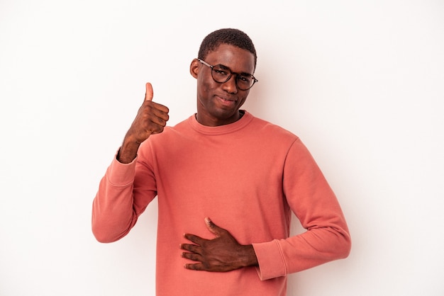 Jeune homme afro-américain isolé sur fond blanc touche le ventre, sourit doucement, concept de manger et de satisfaction.