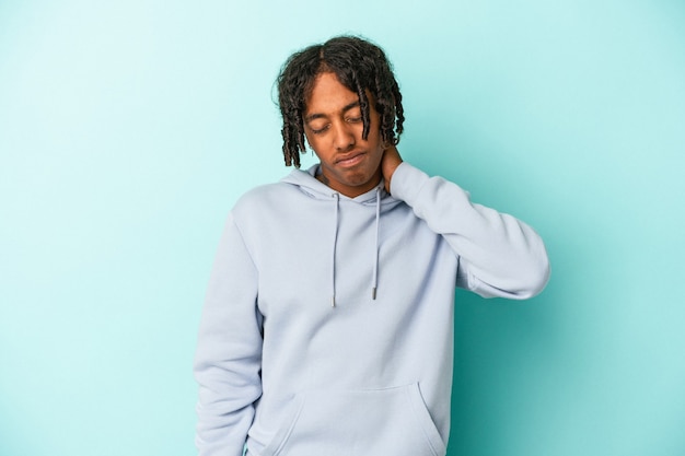 Jeune homme afro-américain isolé sur fond bleu ayant une douleur au cou due au stress, en le massant et en le touchant avec la main.