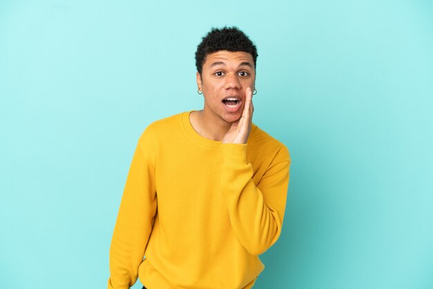 Jeune homme afro-américain isolé sur fond bleu criant avec la bouche grande ouverte