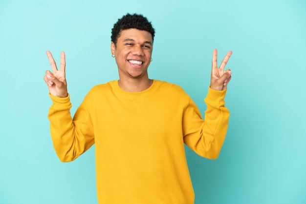 Jeune homme afro-américain isolé sur fond bleu montrant le signe de la victoire avec les deux mains