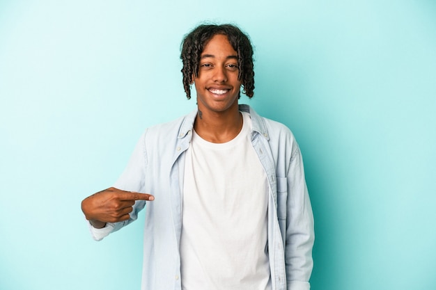 Jeune homme afro-américain isolé sur fond bleu personne pointant à la main vers un espace de copie de chemise, fier et confiant