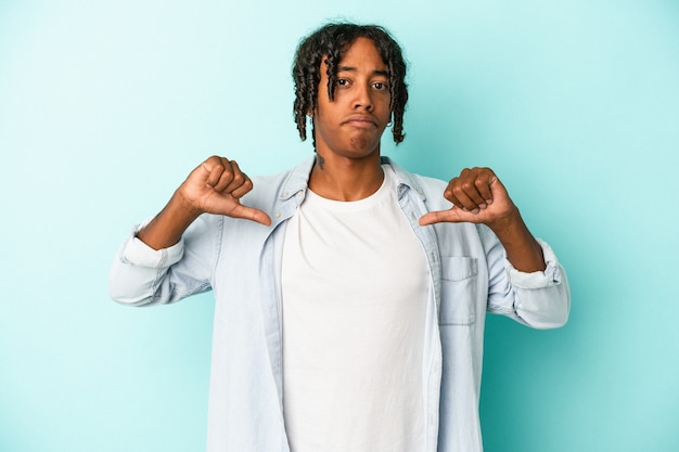 Jeune homme afro-américain isolé sur fond bleu se sent fier et confiant, exemple à suivre.