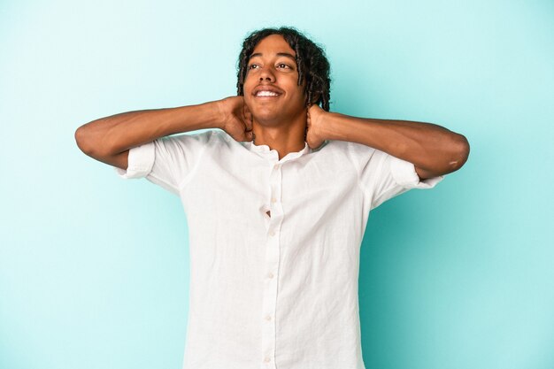 Jeune homme afro-américain isolé sur fond bleu se sentant confiant, les mains derrière la tête.