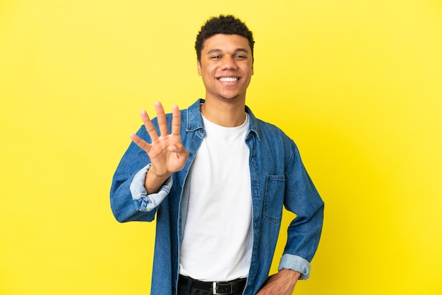 Jeune homme afro-américain isolé sur fond jaune heureux et comptant quatre avec les doigts