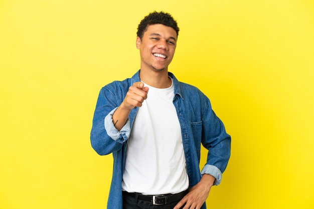 Jeune homme afro-américain isolé sur fond jaune surpris et pointant vers l'avant