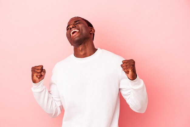 Jeune homme afro-américain isolé sur fond rose célébrant une victoire passion et enthousiasme expression heureuse