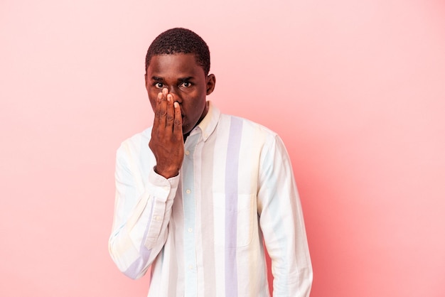 Jeune homme afro-américain isolé sur fond rose choqué, couvrant la bouche avec les mains, soucieux de découvrir quelque chose de nouveau.