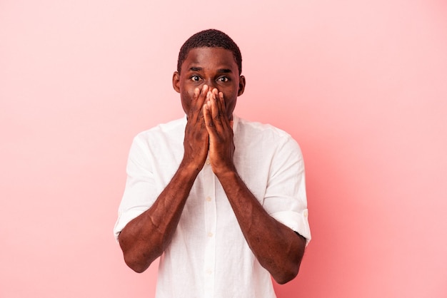 Jeune homme afro-américain isolé sur fond rose choqué couvrant la bouche avec les mains