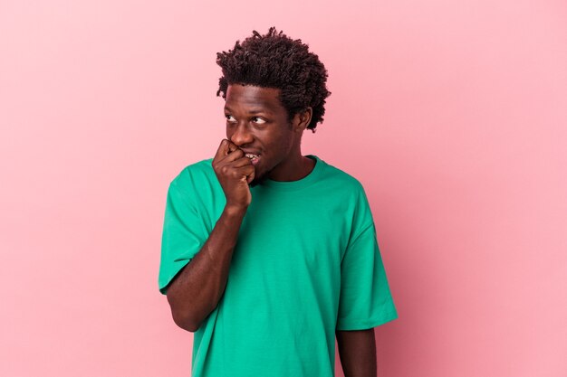 Jeune homme afro-américain isolé sur fond rose détendu en pensant à quelque chose en regardant un espace de copie.