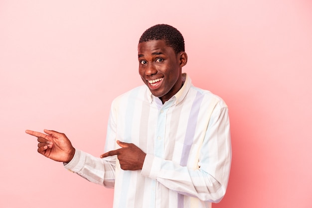 Jeune homme afro-américain isolé sur fond rose excité pointant avec les index loin.