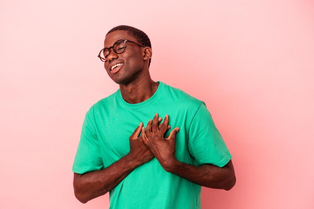 Jeune homme afro-américain isolé sur fond rose a une expression amicale, appuyant la paume contre la poitrine. Notion d'amour.