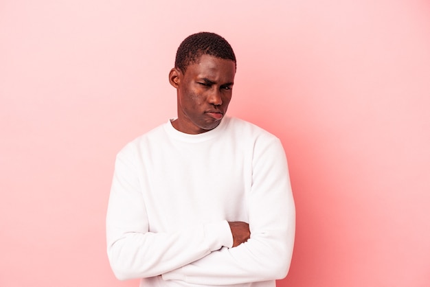 Jeune homme afro-américain isolé sur fond rose malheureux à la recherche à huis clos avec une expression sarcastique.