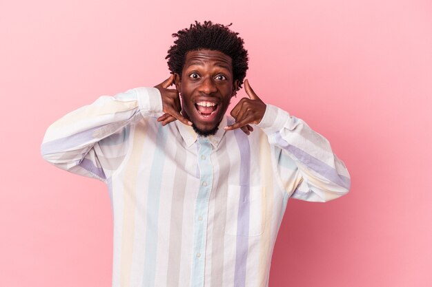 Jeune homme afro-américain isolé sur fond rose montrant un geste d'appel de téléphone portable avec les doigts.