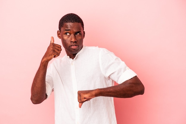 Jeune homme afro-américain isolé sur fond rose montrant les pouces vers le haut et les pouces vers le bas difficile de choisir le concept