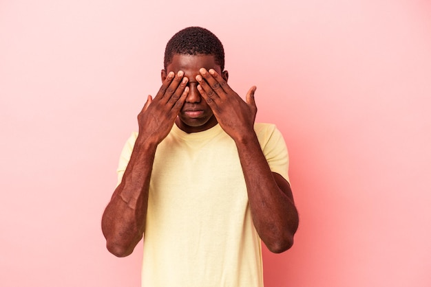 Jeune homme afro-américain isolé sur fond rose peur couvrant les yeux avec les mains