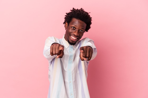 Jeune homme afro-américain isolé sur fond rose pointant vers l'avant avec les doigts.