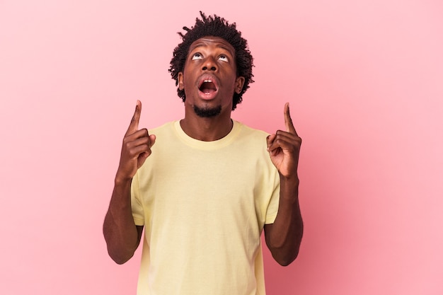 Jeune homme afro-américain isolé sur fond rose pointant vers le haut avec la bouche ouverte.