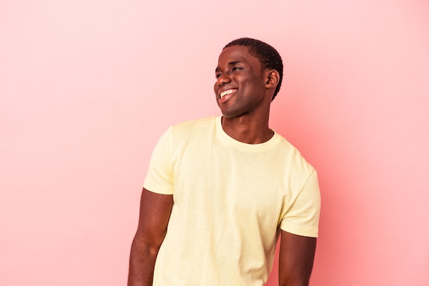 Jeune homme afro-américain isolé sur fond rose riant détendu et heureux, cou tendu montrant les dents.