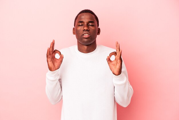 Jeune homme afro-américain isolé sur fond rose se détend après une dure journée de travail, elle fait du yoga.