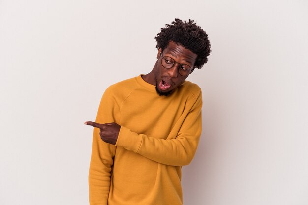 Jeune homme afro-américain isolé sur des points de fond blanc avec le pouce loin, riant et insouciant.