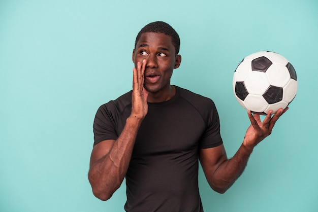 Un jeune homme afro-américain jouant au football isolé sur fond bleu dit une nouvelle secrète sur le freinage à chaud et regarde de côté