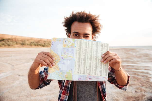 Un jeune homme afro-américain joyeux s'est couvert le visage avec une carte et un clin d'œil