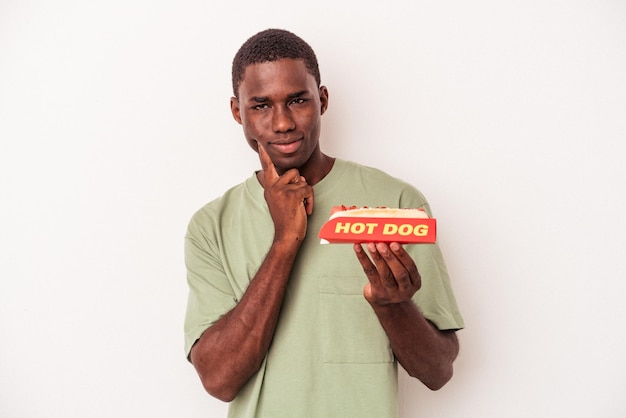 Jeune homme afro-américain mangeant un hot-dog isolé sur fond blanc pointant le temple avec la pensée du doigt concentrée sur une tâche