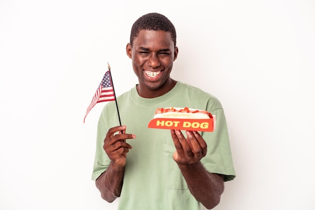 Jeune homme afro-américain mangeant des hot-dogs et tenant le drapeau américain isolé sur fond blanc