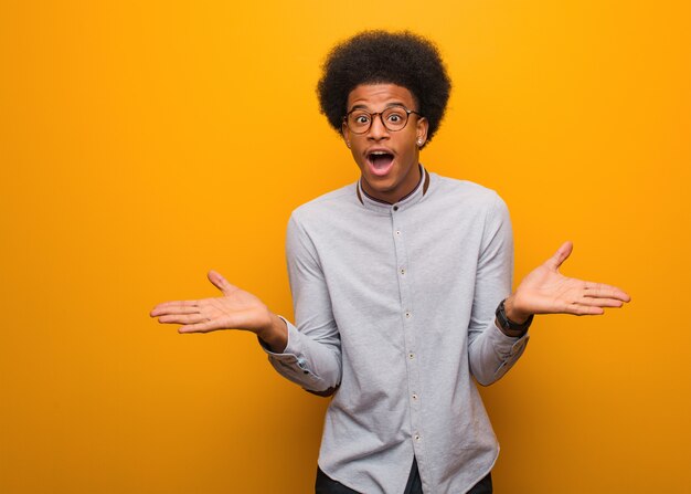 Jeune homme afro-américain sur un mur orange célébrant une victoire ou un succès