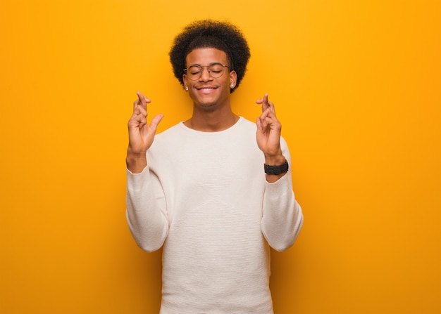 Jeune homme afro-américain sur un mur orange, croisant les doigts pour avoir de la chance