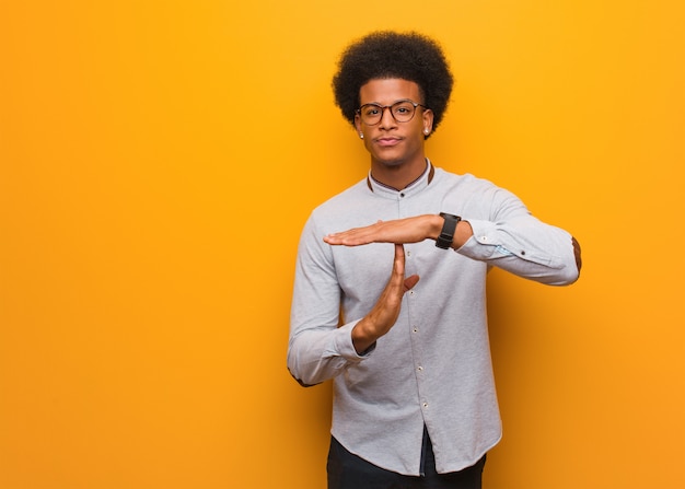 Jeune homme afro-américain sur un mur orange, faisant un geste de délai d'attente