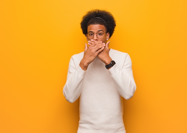 Photo jeune homme afro-américain sur un mur orange surpris et choqué
